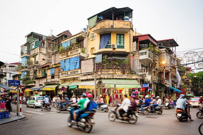 Hanoi. Busy street corner in old town Hanoi, Vietnam. Lots of people are commuting on motorbikes or cars. The street is lined by stores and appartment buildings.
